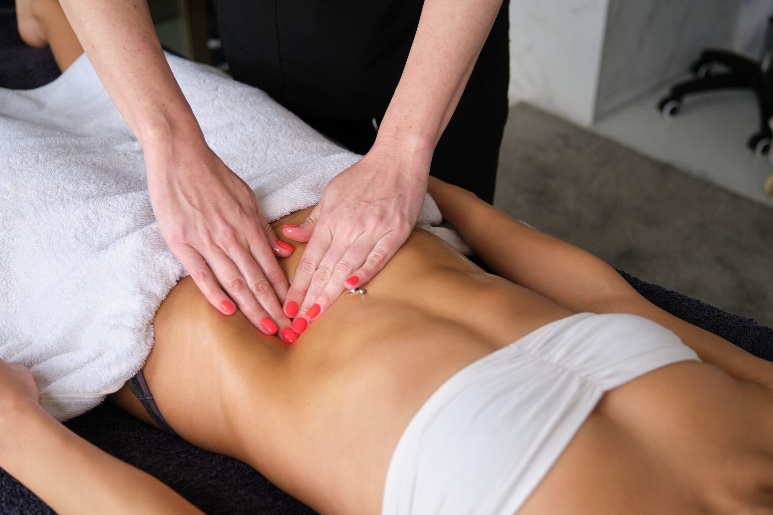 Masseuse massaging abdomen of young woman lying on massage table for Lymphatic Drainage Massage